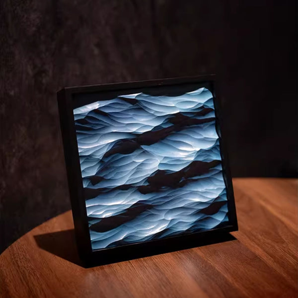 Thin framed artwork with a wavy blue design on a wooden surface