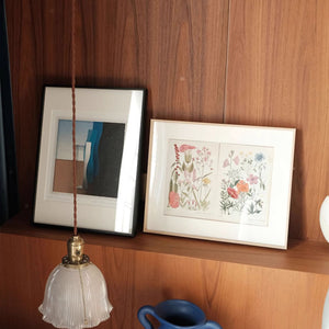 Aluminum alloy picture frames with artwork on a wooden shelf with a pendant light.