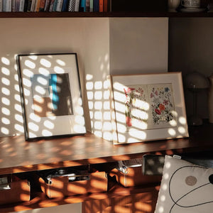 Aluminum picture frames on a wooden surface with sunlight casting shadows.