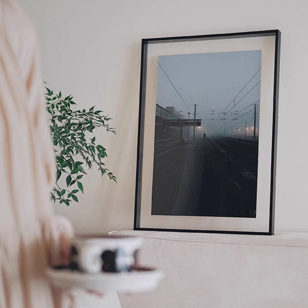 Black acrylic large picture frame with a photograph of a foggy street scene on a wall with a plant and person in the foreground.