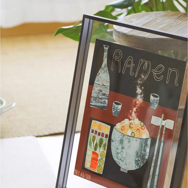 Black acrylic picture framed artwork of a bowl of ramen with chopsticks and a sake bottle on a table