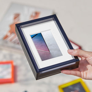 Person holding a graphite colour acrylic picture frame with colorful frames in the background