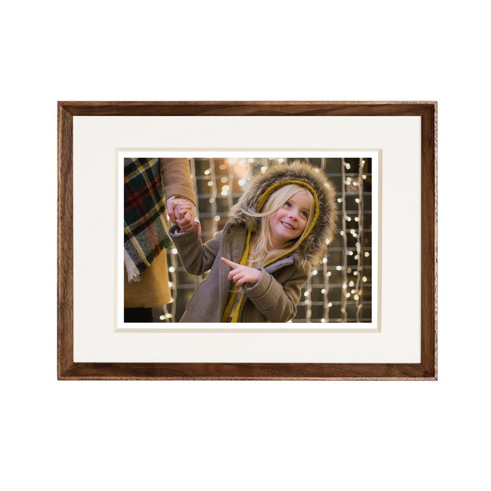Framed photograph of a child in winter clothing with a blurred background. Black walnut beveled frame white background. 
