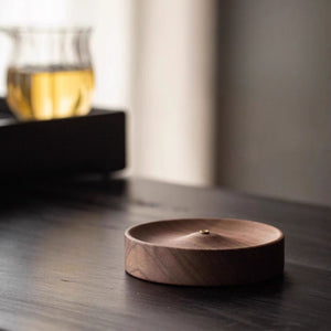 Black walnut incense holder on a dark surface with a blurred glass of tea in the background