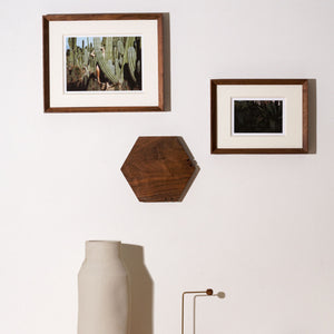 Two framed pictures on a wall with a hexagonal wooden shelf and a vase below. Black walnut picture frame. 
