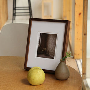Framed photograph on a wooden table with a pear and small vase. Black walnut picture frame. 