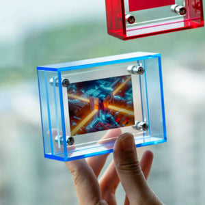Hand holding a transparent blue acrylic picture frame with a colorful display, against a blurred outdoor background