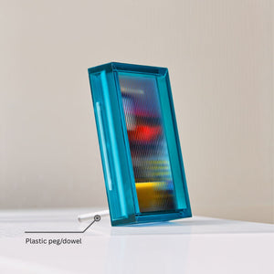 Blue acrylic picture frame with colorful interior on a white surface, featuring a plastic peg or dowel.