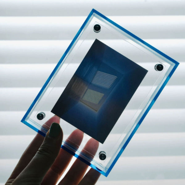 Hand holding a rectangular semiconductor device with a blue frame against a blurred background