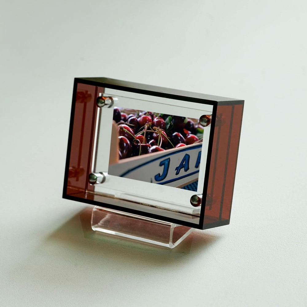 Brown acrylic photo frame with a reflection of cherries and 'JAN' on a white background. 