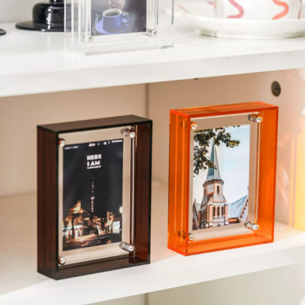 Two acrylic photo frames, one black and one orange, on a shelf. 