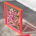 Floral wall art with an electric pink frame on a concrete floor.