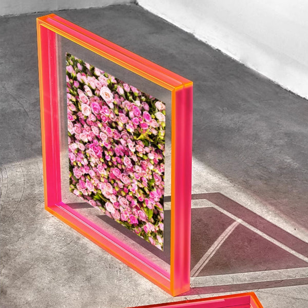 Floral wall art with an electric pink frame on a concrete floor.