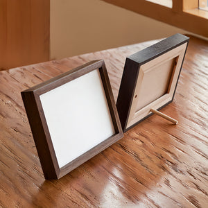 Two wooden picture frames on a wooden surface. Black walnut and Wenge picture frame front and back. Back is beech wood backboard + beech dowel.