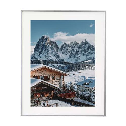 Metal-framed photograph of a snowy mountain landscape with a wooden cabin.