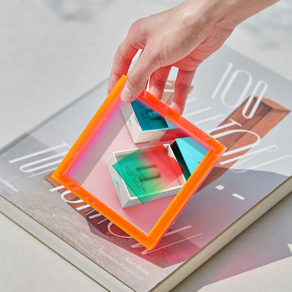 Hand holding a mini electric pink acrylic frame on a magazine