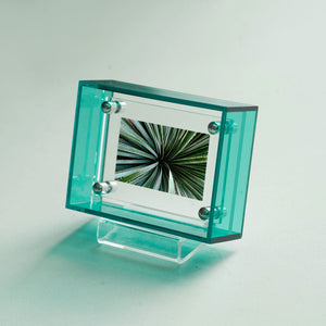 Teal acrylic picture frame displaying an image of a person in a pink dress underwater, on a wooden surface.