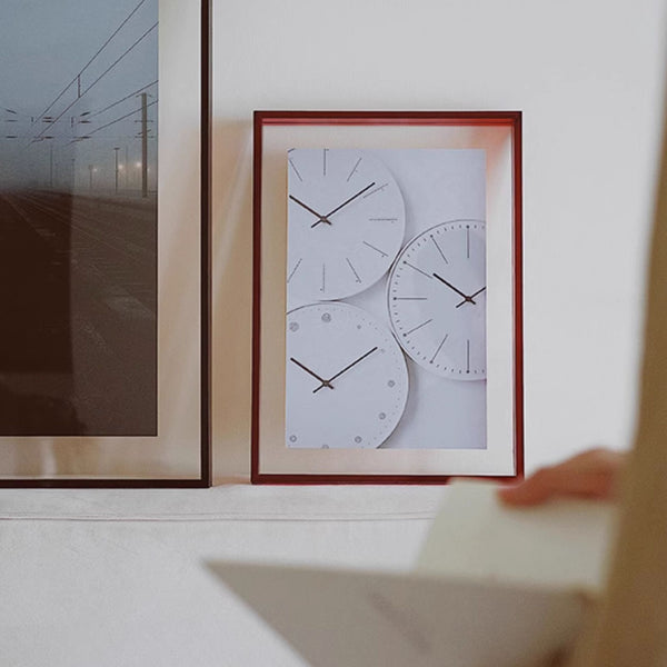 Red framed artwork of three clock faces on a white wall.