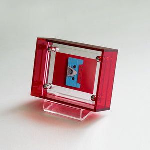 Red acrylic transparent picture frame with a blue cassette tape inside on a white background