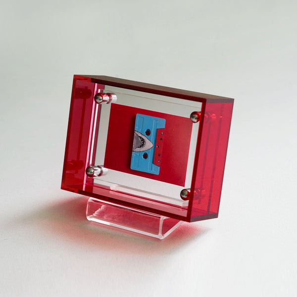 Red acrylic transparent picture frame with a blue cassette tape inside on a white background