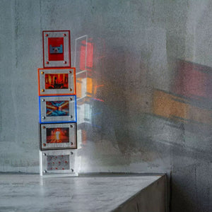 Stack of colorful acrylic picture frames on a textured wall. Red, orange, blue, brown and white.
