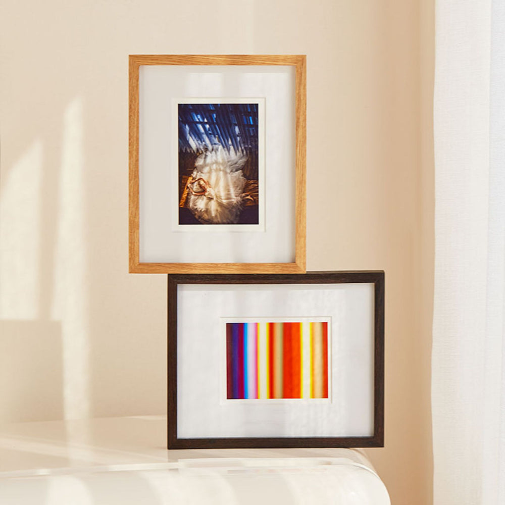 Two framed artworks on a beige wall. Teak and Black Walnut table top picture frames.
