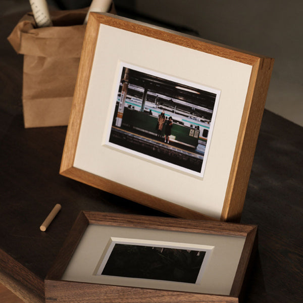 Two wooden picture frames with matted prints on a dark surface. Teak and black walnut picture frame. 