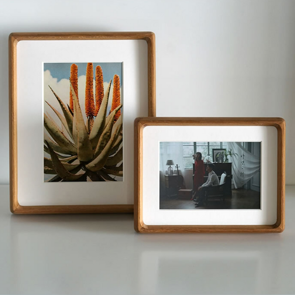 Two wooden teak picture frames with photos of a plant and a living room scene on a white surface.