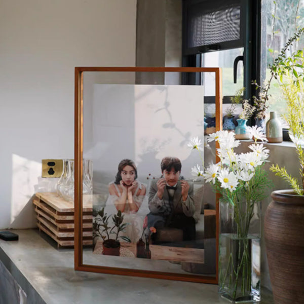 Teak-framed photograph of a couple in a modern living room with plants and decor.