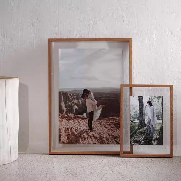 Teak wood transparent frame with photographs of a couple in natural settings on a white wall.