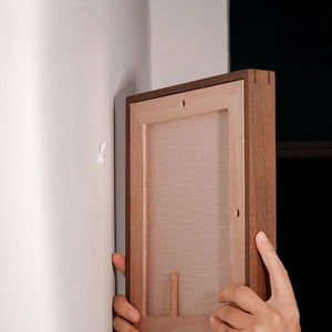 Wooden picture frame held against a white wall. Tenon series frame how to hang on the wall. 