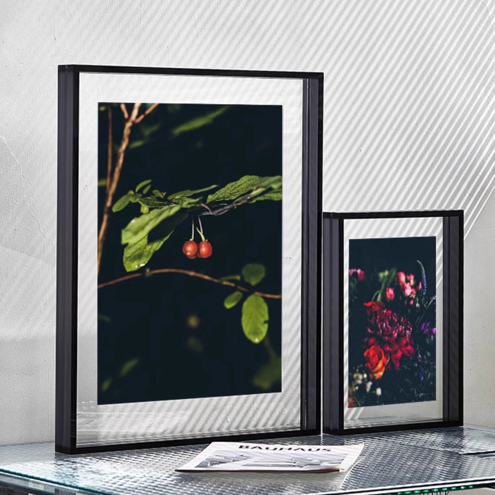 Thick black framed artworks on a glass surface with a magazine underneath.