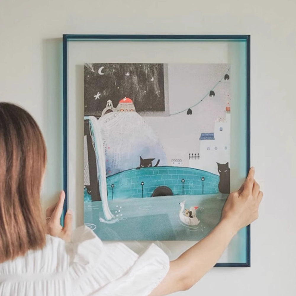 Person holding a thick blue acrylic picture frame illustration of a cat and a dog by a pool at night.