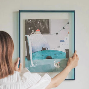 Person holding a thick blue acrylic picture frame illustration of a cat and a dog by a pool at night.