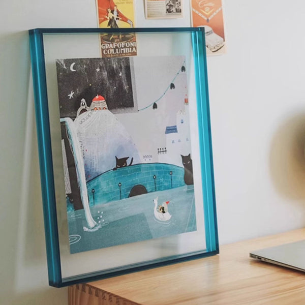 Thick blue picture framed artwork of a snowy scene with a cat and a bird on a desk.