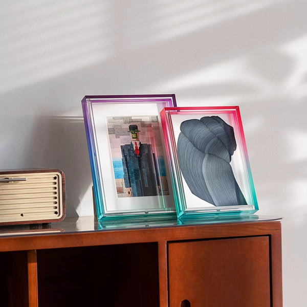 Two ombre acrylic photo frames on a wooden surface with a white wall background