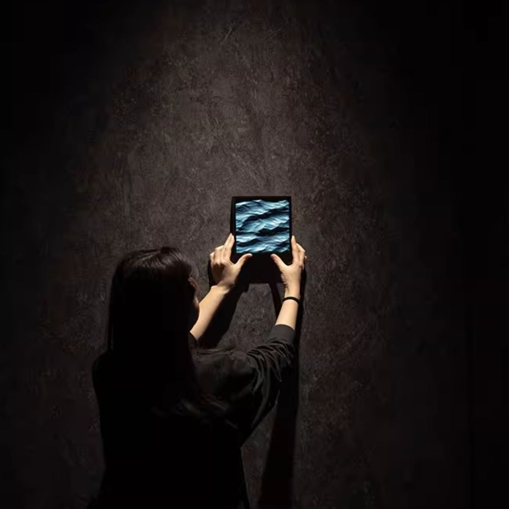 Person holding a small frame with 3D carved blue waves with a dark background