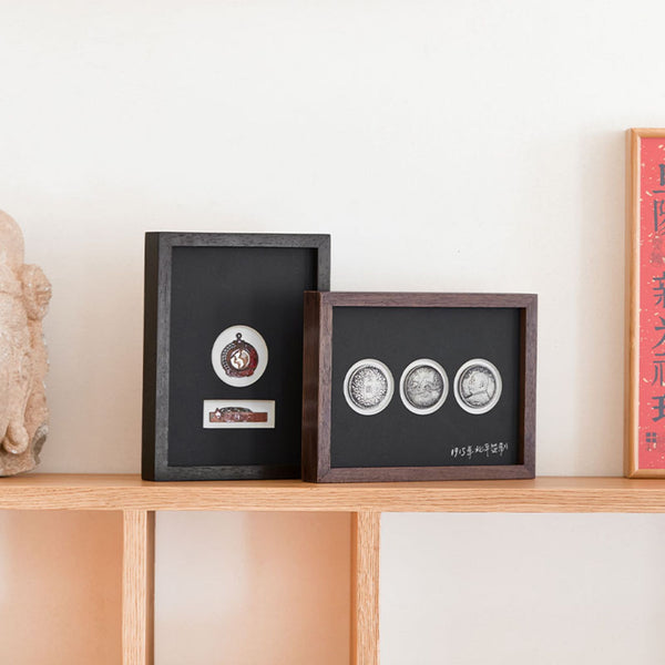 Two framed items on a wooden shelf with a white wall background. Wenge and Black walnut. 