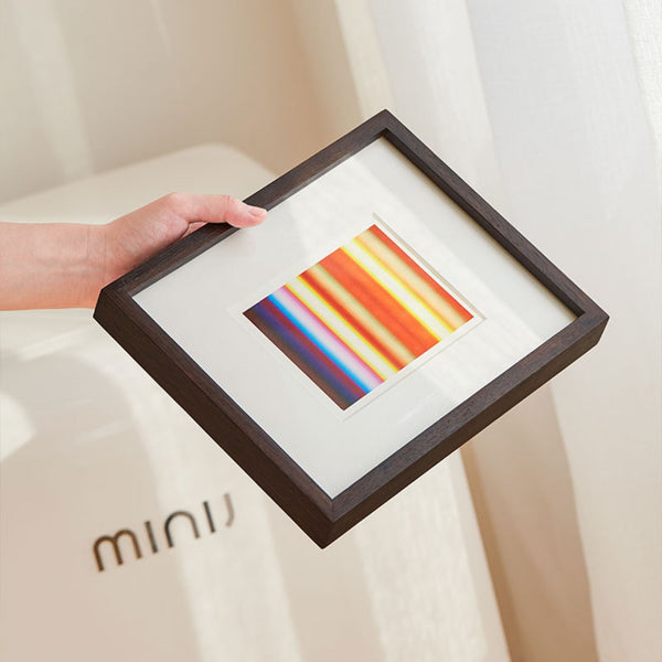Framed artwork with colorful stripes held by a hand on a light background. Wenge wood frame.