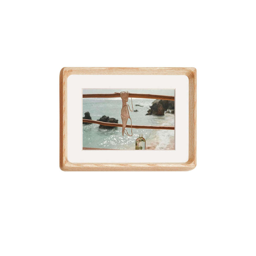 White ash framed artwork of a woman in a swimsuit by the water on a white background