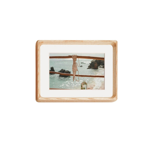 White ash framed artwork of a woman in a swimsuit by the water on a white background