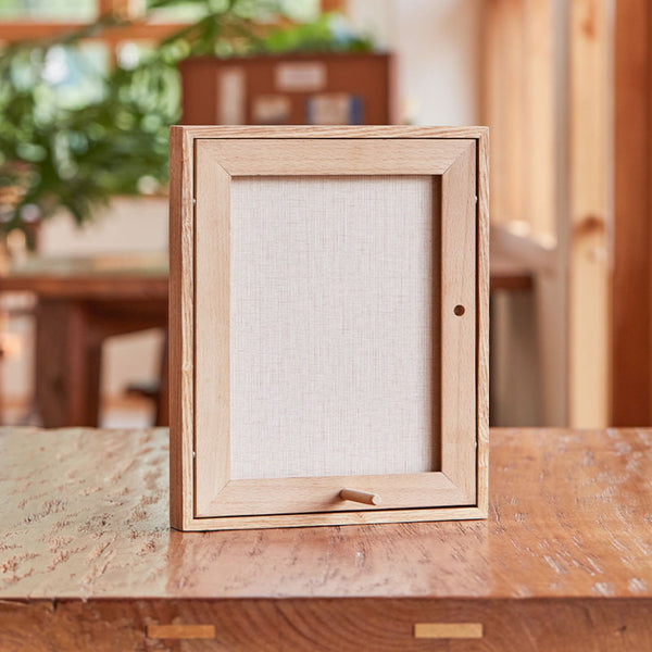 Wooden picture frame on a wooden table with a blurred indoor background. White ash wood frame with Beech wood back board.