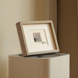 Framed artwork on a stand against a beige wall. White ash wood picture frame. 