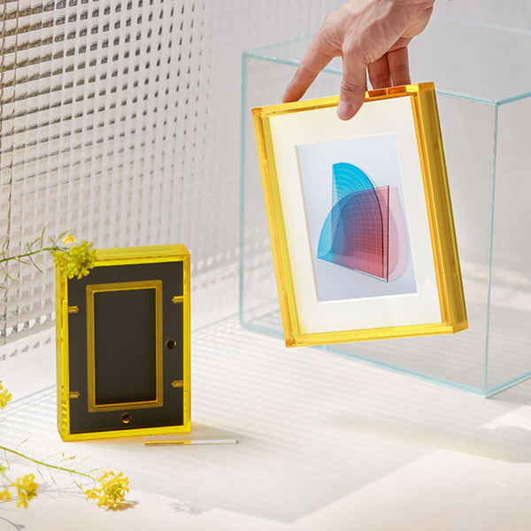 Yellow photo frame with a clear glass cover held by a hand, with a colorful abstract design inside.
