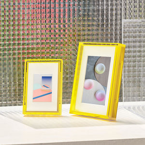 Two yellow-framed artworks on a surface with a textured wall background