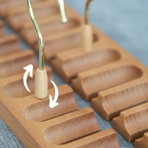 Wooden belt hanger with gold and wooden hook on a gray surface.