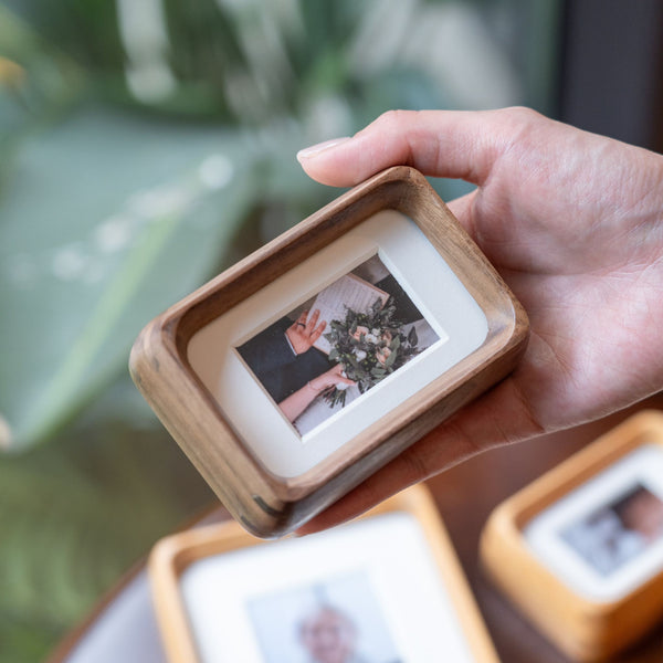 Hand holding a small wooden photo frame with a printed picture of hands holding flowers. wedding specific.