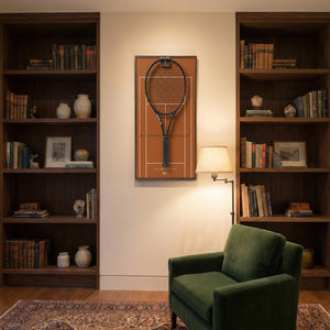 Elegant home library interior showcasing the ONE MAAY French Open clay court tennis racket display mounted on the wall next to a built-in wooden bookshelf and a green reading chair