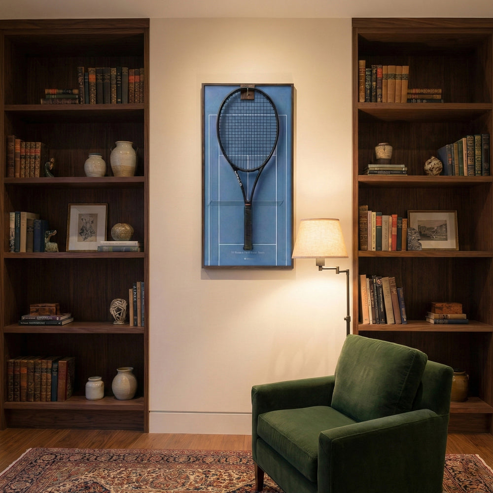 Elegant home library interior showcasing the ONE MAAY Australian Open hard court tennis racket display mounted on the wall next to a built-in wooden bookshelf and a brown leather reading chair.