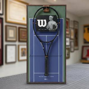 A ONE MAAY US Open-inspired blue hard court tennis racket wall display mounted elegantly next to a wooden bookshelf in a home library, featuring an olive-green side banner that reads "US Open"